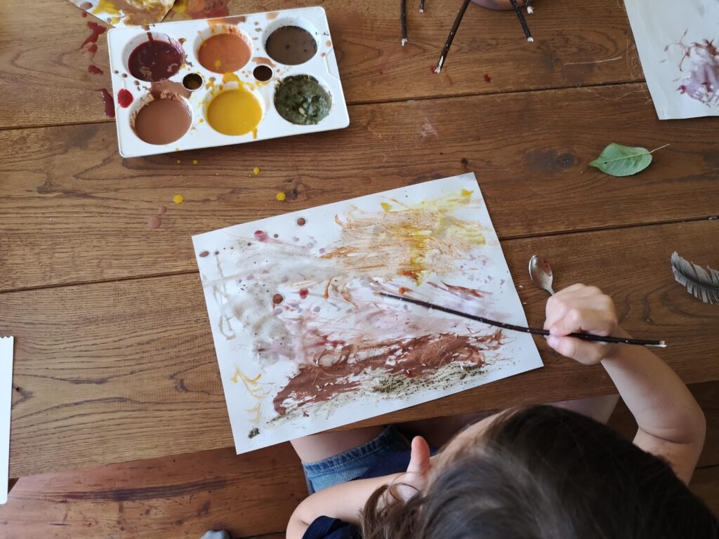 A top-down view of a child painting with natural paints